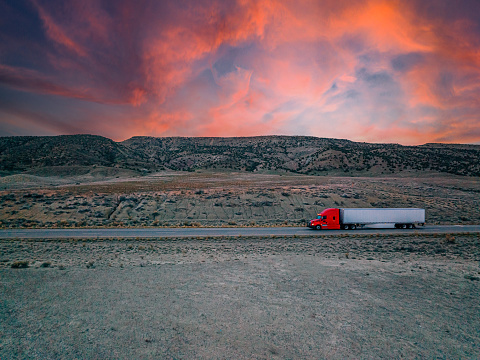 Aerial Drone Shot of a Tractor Trailer Transporting Goods or Product on the Interstate with a Colorful Vibrant Sunrise in a Desert Area near the Utah Colorado Border on Interstate 70