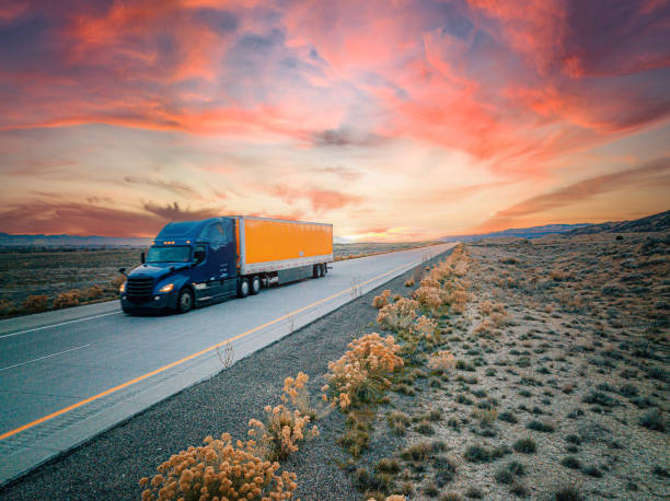 low-angle-luft-drohnenaufnahme eines blauen und orangefarbenen sattelschleppers auf der autobahn mit einem farbenfrohen sonnenuntergang - truck space desert utah stock-fotos und bilder