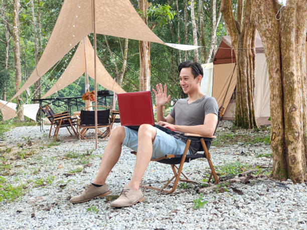 istock Young Asian man using laptop video call while working during his camping vacation in the forest. 1402563751