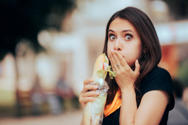 mädchen, das ein ekelhaftes sandwich isst und sich krank fühlt - eating sandwich emotional stress food stock-fotos und bilder