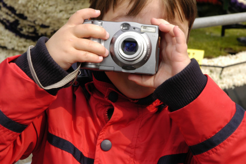 Boy holding a camera and taking pictures of passers by and calling SMILE