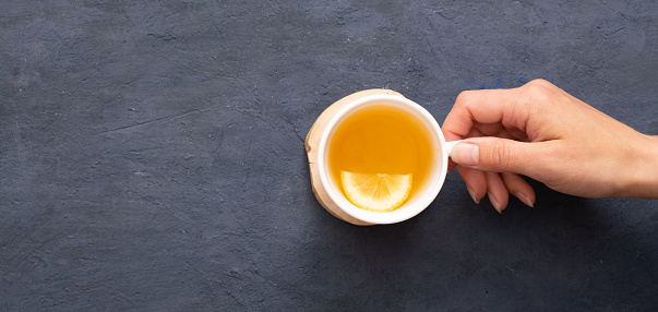 Female hand holding a cup of tea with lemon smile top view on a dark stone background.