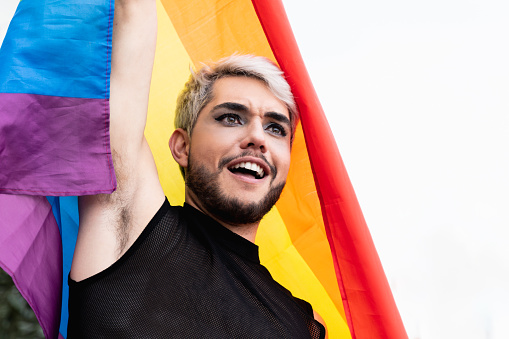 Gay transgender man with makeup holding rainbow flag outdoor - LGBTQ drag queen concept