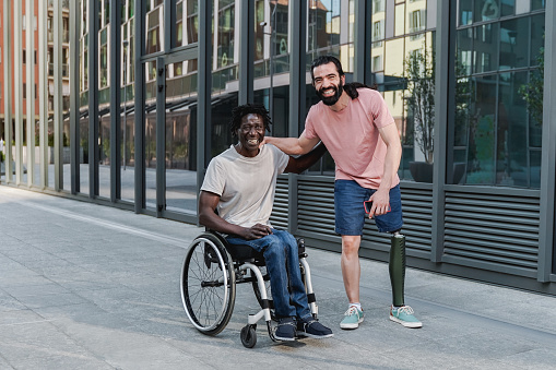 Multiracial friends with disability having fun looking at camera outdoor - Focus on African man sitting on wheelchair