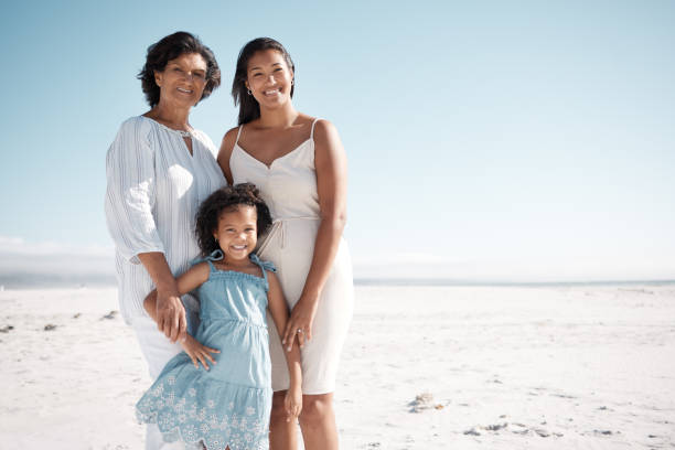 istock Smiling mixed race family standing together on a beach with copyspace. Happy hispanic grandmother bonding with granddaughter over weekend. Adorable little girl enjoying free time with single mother 1402596831