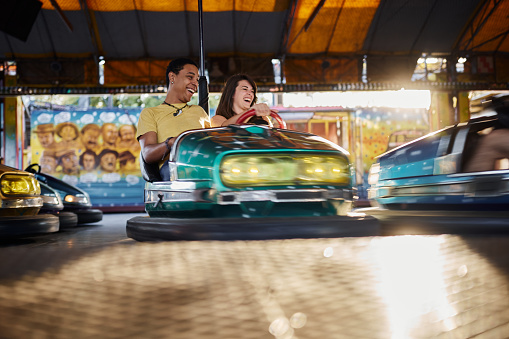 Young carefree couple having fun while driving bumper car at amusement park. Copy space.