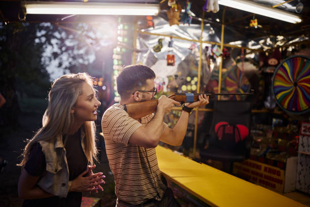 Young happy woman supporting her boyfriend who is aiming at target at amusement park. Focus is on man.