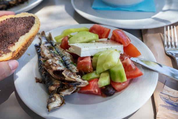 魚のイワシのグリル。新鮮な魚にギリシャサラダを白い皿に盛り付けました。屋外レストランでのグルメシーフードディナー、クレタ島のタベルナ、ギリシャ料理。健康的なライフスタイル� - クレタ島 写真 ストックフォトと画像