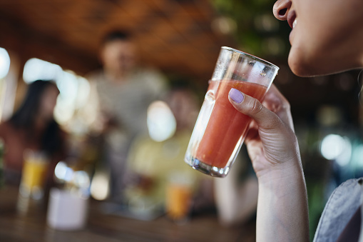 Close up of unrecognizable woman drinking fresh grapefruit juice in a café.