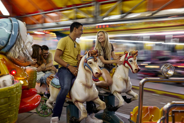 Cheerful couples having fun during carousel ride at amusement park. Blurred motion.