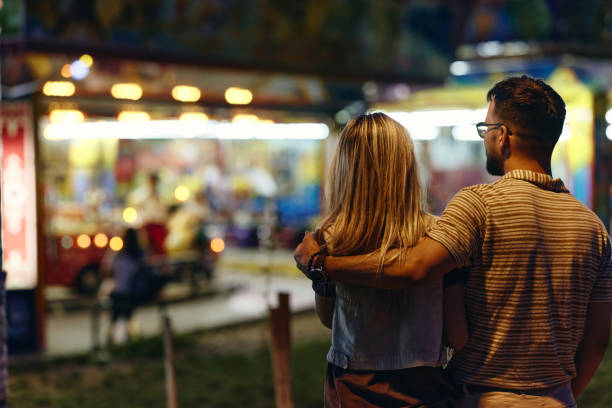 istock Back view of embraced couple during evening at amusement park. 1402597572