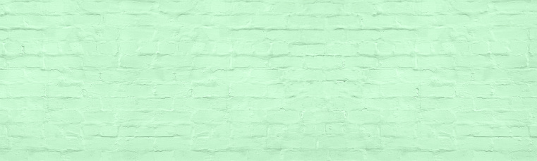 Pistachio color painted old plastered brick wall wide texture. Pastel green rough shabby brickwork. Abstract vintage panoramic background
