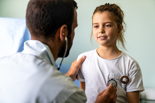 Healthcare medical exam people children and medicine concept. Close up of happy girl and doctor with stethoscope listening to heartbeat