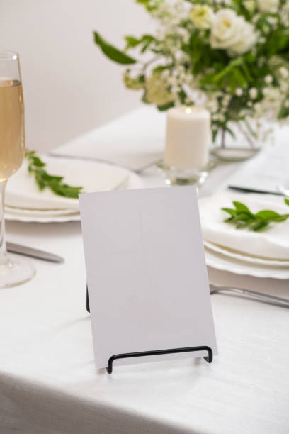 Mockup white blank space card for table number or menu. Wedding teble decoration with white flowers, glasses and white napkins. Elegantly decorated table at a wedding reception. Festive table setting. The wedding decor.