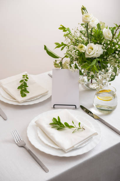 istock Mockup white blank space card for table number or menu. Wedding teble decoration with white flowers, glasses and white napkins. Elegantly decorated table at a wedding reception. Festive table setting. The wedding decor. 1402599889