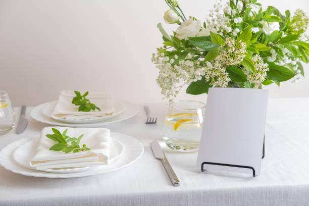 istock Mockup white blank space card for table number or menu. Wedding teble decoration with white flowers, glasses and white napkins. Elegantly decorated table at a wedding reception. Festive table setting. The wedding decor. 1402599904