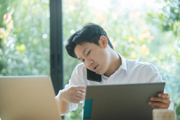 istock Asian man working busy while making phone call and using laptop at home 1402601071