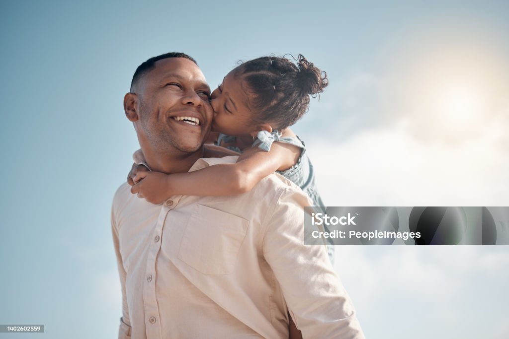Smiling mixed race single father carrying little daughter on piggyback with copyspace. Adorable, happy, hispanic girl bonding with parent and kissing cheek on beach. Man and child enjoying free time Family Stock Photo