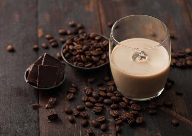 Glass of Irish cream liqueur with coffee beans and dark chocolate in steel bowl on dark wood background. Glass of Irish cream liqueur with coffee beans and dark chocolate in steel bowl on dark wood background. Top view bailey castle stock pictures, royalty-free photos & images