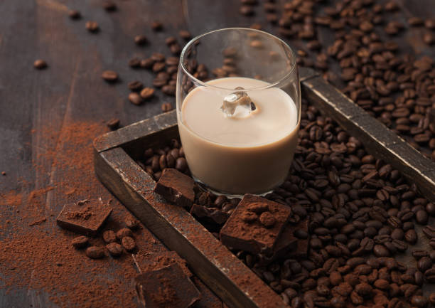 Glass with ice cubes of Irish cream liqueur in wooden tray with coffee beans and powder with dark chocolate on dark wood background. Glass with ice cubes of Irish cream liqueur in wooden tray with coffee beans and powder with dark chocolate on dark wood background. Top view bailey castle photos stock pictures, royalty-free photos & images