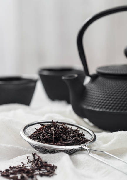 istock Strainer infusor with loose black tea on light cloth background with iron teapot and cups. 1402603118