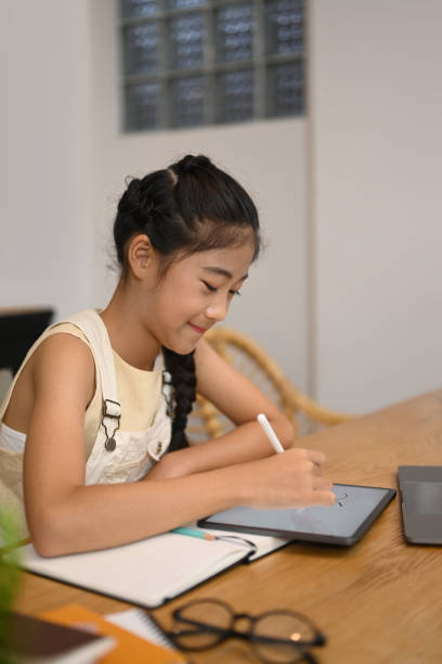 istock Smiling Asian girl doing homework on digital tablet, studying through online learning system. 1402603285