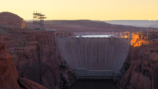 Glen Canyon Dam with Glen Canyon Dam Bridge in front and Lake Powell water surface in the back in the golden hour light. Red cliffs of the gorge and concrete wall of the dam in tranquil scene