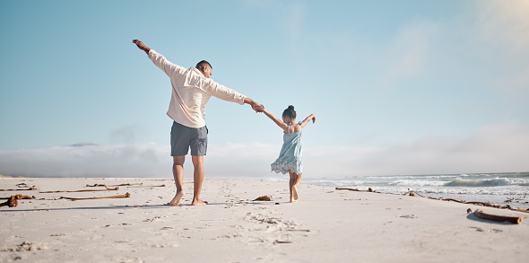 Full length rearview of unknown mixed race single father holding little daughter’s hand with copyspace. Adorable, hispanic girl walking and bonding with parent. Man and child enjoying beach free time