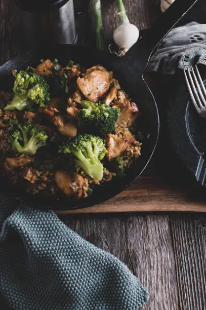 Healthy body building meal with pan fried chicken breast, brown rice and broccoli. Served in a rustic iron pan on wooden table background with copy space. Top view
