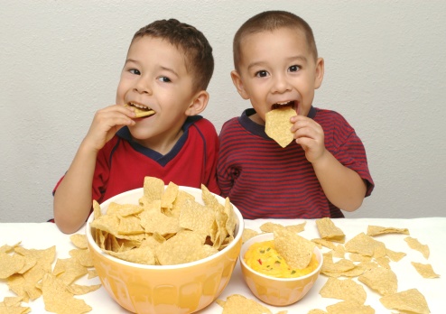 Two brothers aged 4 and 5 years old enjoy a huge bowl of tortilla chips with queso