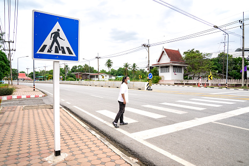 Asian man looks to vehicle on the road, he waits for sure to  across crosswalk to the other side, Thailand.