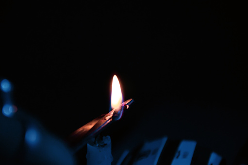 Closeup of a candle light fire in dark night. Candle fire separated from wax by a wooden stick. Fire flame of candle thread on the wood illuminating the dark.