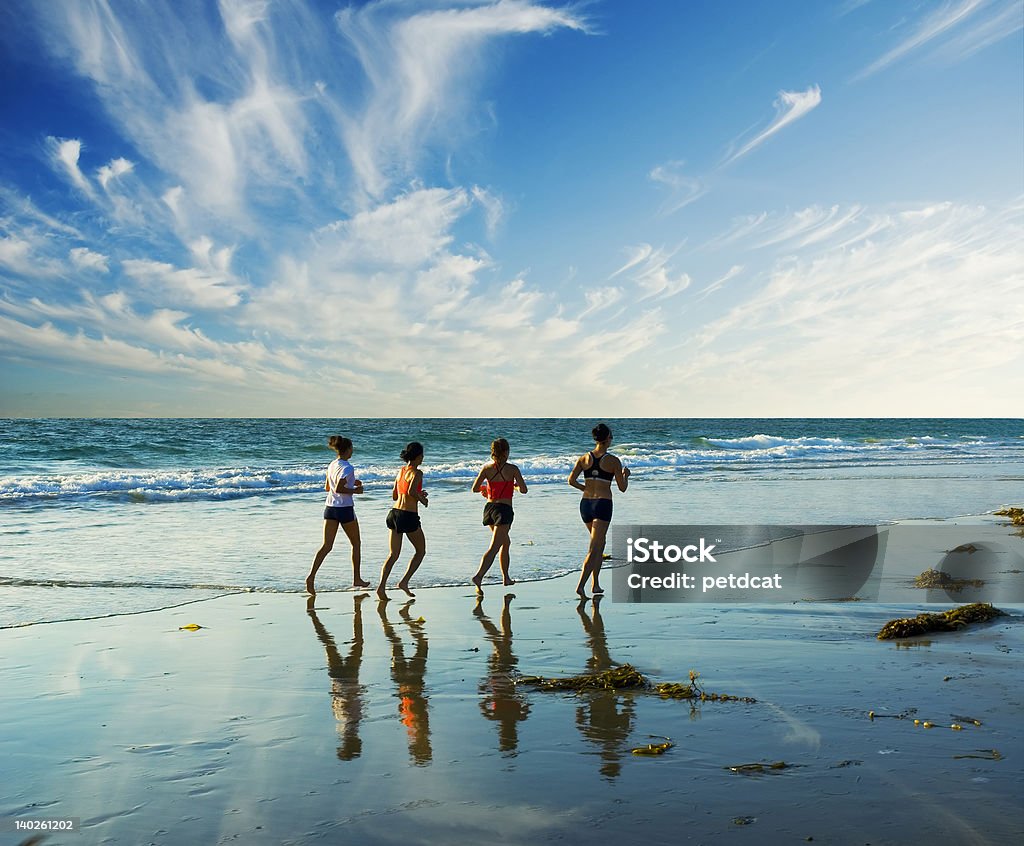 jogging along the surf four women go jogging on the beach along the waters edge Active Lifestyle Stock Photo