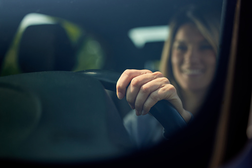 Close up of woman's hand on steering wheel while going on a trip by car. The view is through glass.