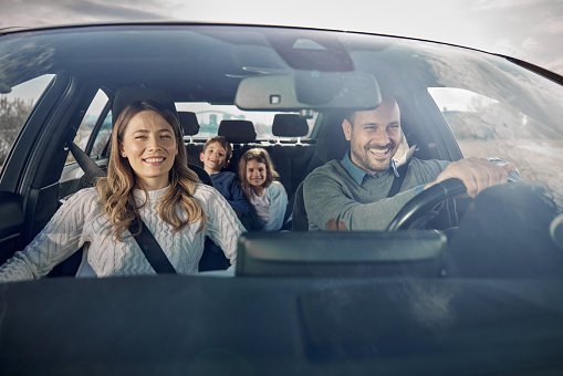 Happy parents and their kids having fun while going on a trip by car. The view is through glass.