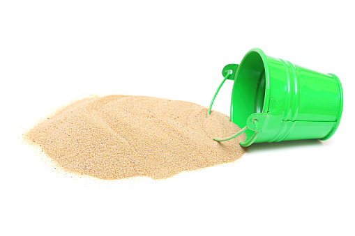 Pile of dry sand and miniature green bucket isolated on white background.