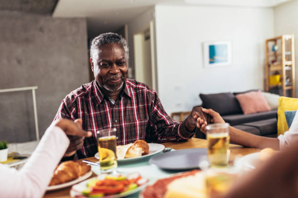 何世代にもわたるアフリカ系アメリカ人の家族が夕食のテーブルで優雅さを語り、手をつないだ - praying saying grace dinner meal ストックフォトと画像