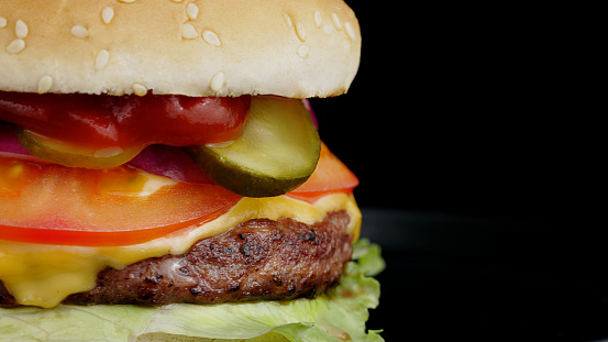 Beef burger with cheese on the black plate on black background, close-up, panoramic view.