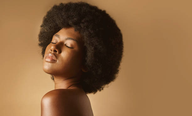 istock Confident African American woman with a natural afro posing against brown studio copyspace background. Young beautiful black female model looking trendy, powerful and sensual with smooth glowing skin 1402615936