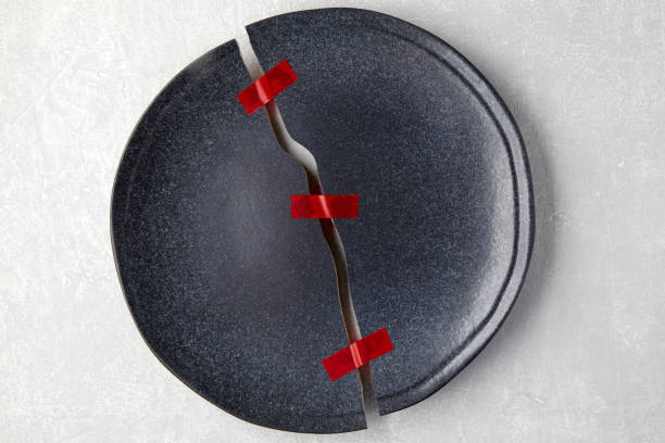 Broken plate is red taped together on a light gray concrete table. Restoration of relations