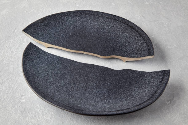 istock Two halves of a broken dark ceramic plate on a light gray concrete table 1402618013