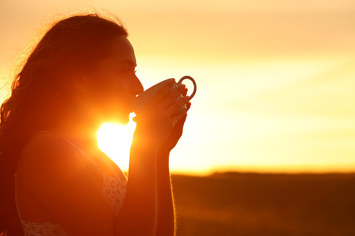 Woman silhouette drinking coffee at sunset