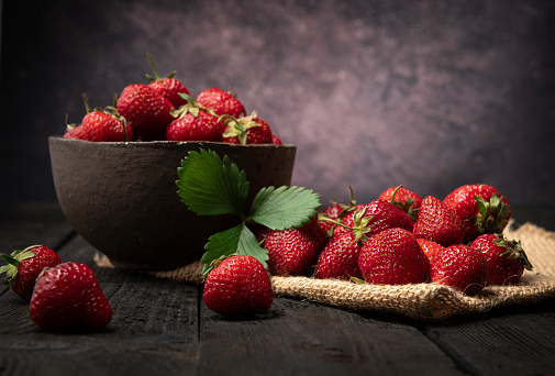 fresh strawberries in a bowl on wooden dark table.