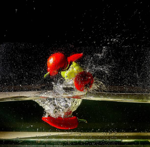 i frutti cadono nell'acqua su uno sfondo nero - pepper vegetable red green foto e immagini stock