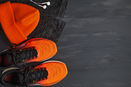 Orange sneakers, orange knitted hat, warm running leggings on a dark wooden table. Cold running equipment