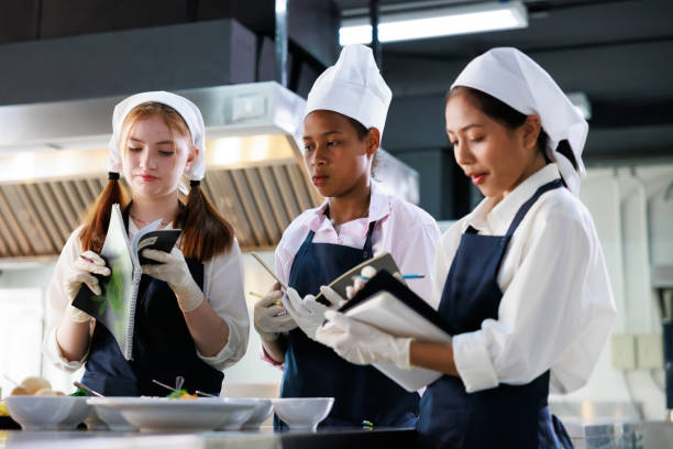 istock take note on book. Cooking class. culinary classroom. group of happy young woman multi-ethnic students are focusing on cooking lessons in a cooking school. 1402628357