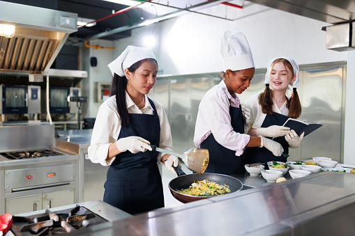 take note on book. Cooking class. culinary classroom. group of happy young woman multi-ethnic students are focusing on cooking lessons in a cooking school.