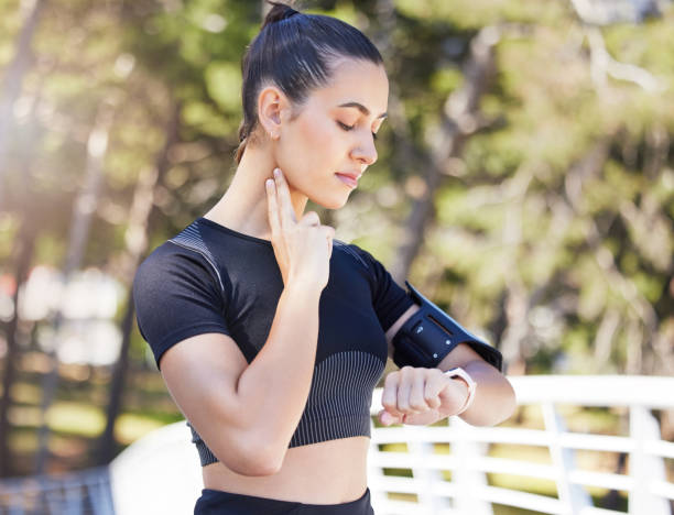 Young sportswoman resting after her workout and checking her pulse while looking at her smart watch and monitoring heart rate by placing two fingers on her neck Young sportswoman resting after her workout and checking her pulse while looking at her smart watch and monitoring heart rate by placing two fingers on her neck cardiac conduction system stock pictures, royalty-free photos & images