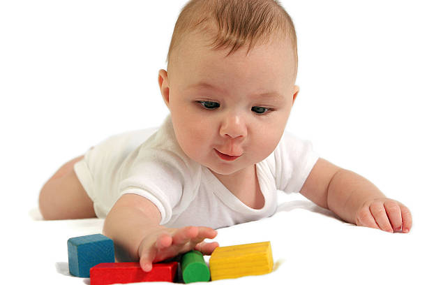 A baby dressed in white reaching for colorful blocks Baby reaching for colorful wooden blocks five animals stock pictures, royalty-free photos & images