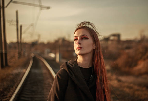 Young lonely woman walking along railway track, on background of industrial city, in dramatic and anti-utopia style Young lonely woman walking along a railway track, on the background of an industrial city, in dramatic and anti-utopia style cinematic music photos stock pictures, royalty-free photos & images